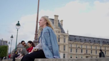 Paris 'teki Louvre Müzesi' nin yakınında güneşli bir günün tadını çıkaran kot ceketli Ukraynalı genç bir kadının yavaş çekim videosu. Yüksek kalite 4k görüntü