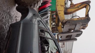 Forklift arabaları hurdalığa yığar çatal temizleme araçlarıyla yakınlaştırır. Bir buldozer bozuk bir arabayı yağmurlu havada, ağır çekimde çöp sahasında hareket ettirir. Dikey görünüm. 4k