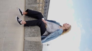 Paris 'teki Louvre Müzesi' nin yakınında güneşli bir günün tadını çıkaran kot ceketli Ukraynalı genç bir kadının yavaş çekim videosu. Dikey video. Yüksek kalite 4k görüntü