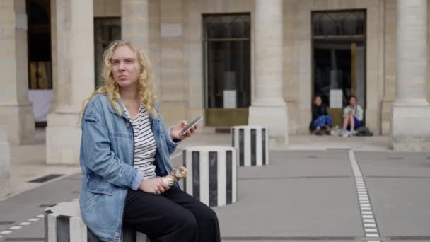 금발의 머리카락과 자켓을 여자는 파리의 광장에 휴대전화로 뭔가를 있습니다 루브르 — 비디오