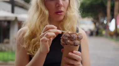 Tuhaf bir jest olarak, bir kadın elini ve kaşığını kullanarak nazikçe waffle külahında dondurma yer. Baş ve parmakları çenesinin yanında senkronize çalışıyor. Ağır çekim. Dikey görünüm. Yüksek kalite 4k