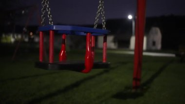 Otlar ve bitkilerle çevrili bir salıncak gece yarısı bir şehir parkında boş duruyor. Şehir ışıklarının elektrik mavisi karanlığa zıt düşer ve dingin bir dinlenme noktası yaratır. 4k