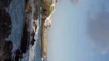 Okyanusa bakan bir uçurum, arka planda bir bina ve bulutlarla dolu güzel bir gökyüzü. Tenerife, dikey video. Yavaş çekim