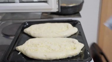 Genç kız fırına içinde çiğ khachapuri olan bir yemek örtüsü koyar. Gürcistan yemekleri, Adjarian Khachapuri. Fırınla yemek pişirmek. Peynirli hamur pişirmek. Yüksek kalite 4k görüntü