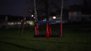 Otlar ve bitkilerle çevrili bir salıncak gece yarısı bir şehir parkında boş duruyor. Şehir ışıklarının elektrik mavisi karanlığa zıt düşer ve dingin bir dinlenme noktası yaratır. 4k