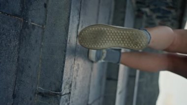 Dişi bacaklar yakın plan, bulutlu bir günde bir kız merdivenleri tırmanır. Dikey görüntü, Ağır çekim 4k. Ayaklarının ve bacaklarının yakın çekimleri ve fayanslı zeminde duruşu