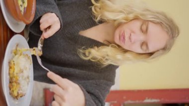 Bir kadın lezzetli yemekler yemek için çatal kullanarak masada yemeğin tadını çıkarıyor. Zarif jestleri taze malzemeler ve sebzelerle pişirme sanatını gözler önüne seriyor. Dikey video. Yavaş çekim 4k