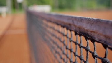 Bir tenis sahasında, ahşap çitler, tuğla işçiliği ve tel örgülerle çevrili bir tenis ağı. Manzarada ahşap leke, ahşap ve toprak bulunur. Yavaş çekim