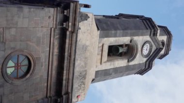 Üzerinde bir zil olan, parlak mavi gökyüzüne karşı kurulmuş bir saat kulesi. Kule zarif tasarımı ve tarihi cazibesiyle çarpıcı bir etki yaratıyor. Tenerife. İspanya. Dikey video 4k
