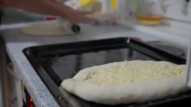 Peynirli ekmek hamurunun yakın plan çekimi, arka planda elleri olan bir ev mutfağında, fırın tepsisi üzerinde hazırlanıyor..