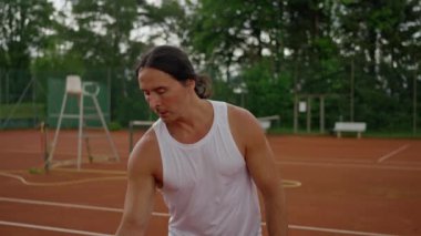 Bir adam kil sahada tenis oynayarak, atletizm ve tutku sergileyerek yetenek ve adanmışlık gösteriyor. Yavaş çekim