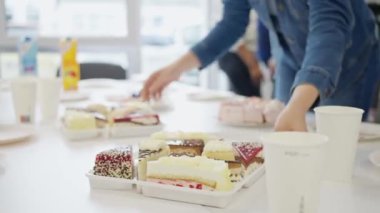 Bir kişi ofis kutlaması için masa üzerinde iş arkadaşlarıyla renkli tatlılar hazırlıyor.