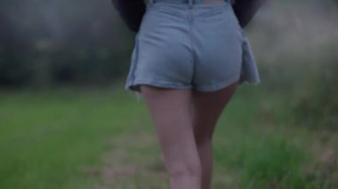 Sakin doğal ortam, kot şortlu kadın çimenli yolda yürüyor, doğada sükunet ve güzellik yayıyor.