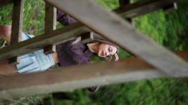 Genç bir kadın yemyeşil yemyeşil kırsal bir ahşap yapının altında dururken doğanın tadını çıkarıyor. Ağır çekim. Dikey video