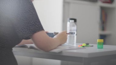 Bir insan, yanında fosforlu kalemler, kitap ve su şişesi olan bir masada ders çalışmaya odaklanır.