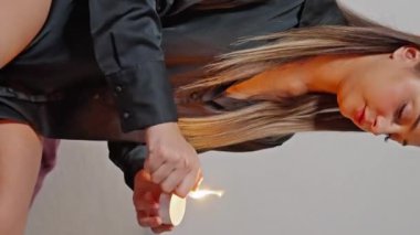 Çıplak vücudunun üzerinde siyah gömlekli ve katmanlı saçlı kadın elinde bir mum tutarak yere oturur ve onu ateşe verir. Dikey video. Yüksek kalite 4k