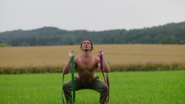 Üstsüz bir adam tepeler ve ağaçlarla çevrili pitoresk bir alanda direniş bandı çalıyor. Yavaş çekim 4k