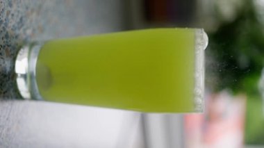 Tezgahın üzerinde bulunan uzun bir bardakta canlı yeşil bir içeceğin yakın çekimi canlandırıcı bir titreşim yakalıyor. Dikey video. Yavaş çekim