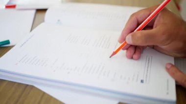 Odaklanmış bir öğrenci, çalışmayı geliştirmek için turuncu bir kalemle Wellorganize edilmiş bir deftere detaylı notlar yazar. Kalemle yakın çekim.