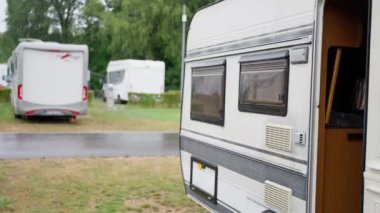 Huzurlu bir ortamda, birkaç kamp aracı canlı, yemyeşil bir kamp yerinde güzel bir şekilde düzenlenir.