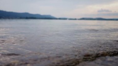 Sakin bir kıyı şeridi, bulutlu bir gökyüzünün altında kumlara doğru süzülen yumuşak dalgalar, sakinlik ve gevşemeyi çağrıştırıyor. Yavaş çekim