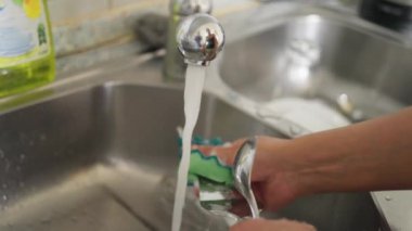 Bir birey, akan suyun altında sabun kullanırken mutfak lavabosunda özenle bulaşıkları yıkıyor.