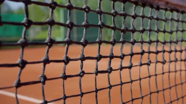 Korttaki ahşap çerçeveye gerilmiş tel örgülerden yapılmış tenis ağının detaylı bir görüntüsü bulanık bir arkaplanda kadın raketle tenis topuna vuruyor, ağır çekimde. Yüksek kalite