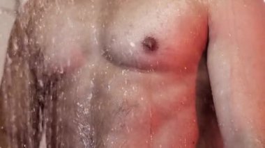 Duşta çıplak erkek gövdesi. Duşta parlayan su damlacıklarını ve neşeli bir atmosferi aydınlatan bir figür. Yavaş çekim