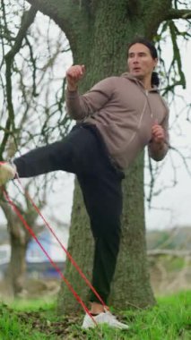 Kararlı ve odaklanmış bir sporcu direnç bantları kullanarak bir ağaca karşı esneme egzersizi yapıyor.