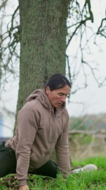 Bir adam gerinir, yarılır, doğada, sonbaharda, büyük bir ağacın altında. Açık hava Yoga Pozisyonları, farkındalık ve Gevşeme Tekniklerini Geliştirmek için kullanılıyor. Yüksek kalite 4k görüntü