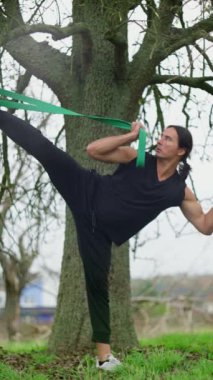 Bireyler, doğadayken bir direniş bandını kullanarak dinamik bir esneme egzersizine girişiyor. Etkili bir Açık Hava Fitness rutini. Daha Sağlıklı Olmak İçin Direniş Bantlarıyla gösteri yapın. 4k