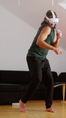 Adam modern, şık bir oturma odasında VR kulaklık ve kumandayla oyun oynamakla derinden ilgileniyor. Bir insan sanal boks kaskında pratik yapıyor. Yavaş çekim 4k görüntü