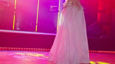 Büyüleyici ve zarif bir dansçı, canlı sahne ışıklarının arasında güzel, dalgalı bir elbiseyle zarifçe döner.