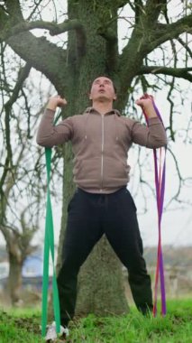 Parkta egzersiz yapan bir adam, direniş bantlarını kullanarak güçlü bir eğitim alıyor.