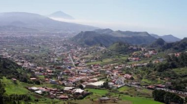 Dağlarla çevrili yemyeşil bir vadinin nefes kesici panoramik manzarası ve altında canlı bir topluluk..