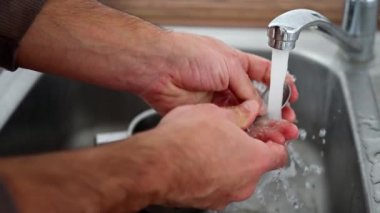 Mutfak lavabosunda sürekli akan bir su akışı altında çok sayıda çatalı özenle ve özenle temizleyen bir kişi. Yavaş çekim 4k