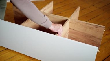 Bir kişi ahşap bir mobilya tabanını özenle birleştiriyor, rahat bir iç mekanda çeşitli aletlerden faydalanıyor. Mobilya Yapımı Güçlü Ahşap Üssü İnce Kurmanın Ayrıntılı Süreci