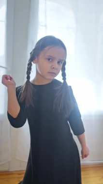 Güzel örgüleri olan genç bir kız şık siyah bir elbiseyle canlı bir arkaplana karşı güven içinde poz veriyor. yavaş çekim