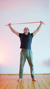 Kendini adamış bir fitness meraklısı, kapalı bir ortamda direnç bandı kullanarak esneme hareketleri yapıyor.