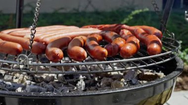 Lezzetli sosisler barbekü ızgarasında cızırdıyor yaz piknikleri ve dostça toplantılar için mükemmel bir yemek hazırlıyorlar.