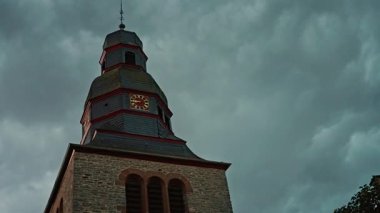 Bulutlu akşam gökyüzünde, Protestan Kilisesi 'nin üzerinde gök gürültüsü ve şimşek. Dengesiz, bulutlu bir gökyüzünün altındaki eski bir saat kulesinin yukarıdan görünüşü, tarihi mimari ve zamansız güzelliği gözler önüne seriyor. 4k