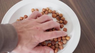 Bir el, beyaz bir tabaktan fındık almak için uzanır ve mükemmel bir yemek etkileşimi anını yakalar.