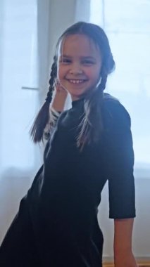 Büyüleyici siyah elbiseli neşeli küçük bir kız neşeyle dans ediyor parlak, aydınlık bir odada