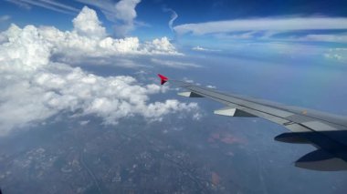 Pofuduk bulutların ve canlı mavi gökyüzünün üzerinde süzülen bir kanadı güzel gösteren nefes kesici bir hava manzarası.