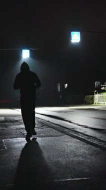 Issız bir yolda sessizce koşan yalnız bir figür, sokak ışıklarının hafif ışığıyla sessizce aydınlatılıyor. Yavaş çekim