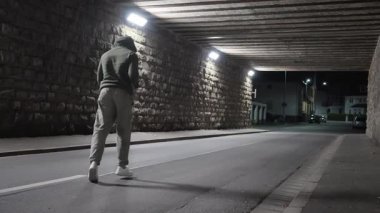 Yalnız bir koşucu geceleri karanlık bir şehir geçidinde hızla ilerler, kararlılık ve enerji gösterir.