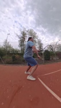 Yetenekli bir oyuncu, bulutlu bir gökyüzünün altında kil sahada yapılan gergin bir tenis maçında olağanüstü bir atletizm sergiliyor.