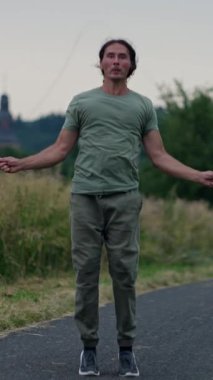 Atletik bir adam atlama halatı egzersizleri yapıyor. Manzaralı bir yolda, çeviklik ve zindelik sergiliyor..