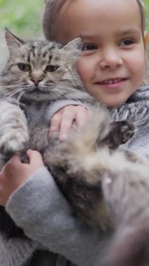 Neşeli ve kaygısız bir çocuk dışarıda güneşli güzel bir günün tadını çıkarırken tüylü bir kediyi neşeyle tutuyor.