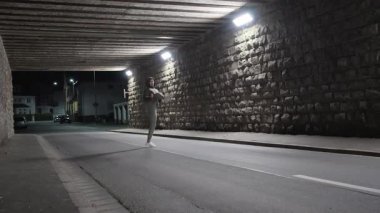 Yanlız bir insan gece aydınlık bir tünelde koşar, canlı kentsel fitness kültürünü vurgular.